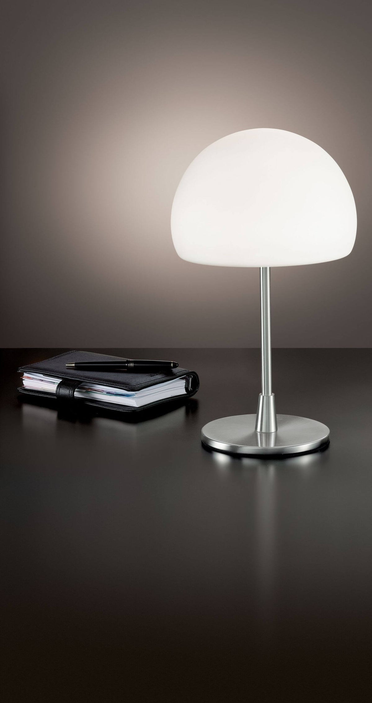 Mise en ambiance sur bureau sombre avec carnet et stylo, lampe allumée.