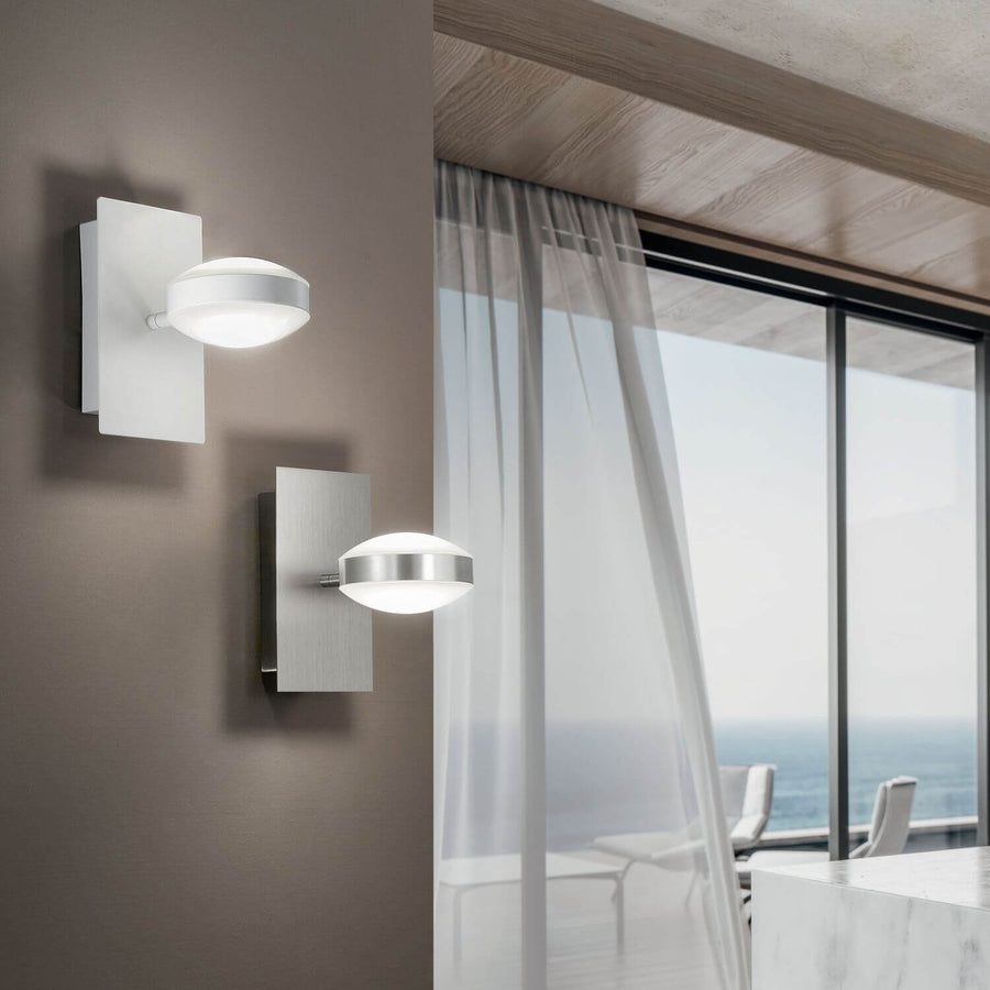 Deux appliques murales allumées dans un intérieur contemporain, l'une blanche, l'autre chromée, vue sur la mer