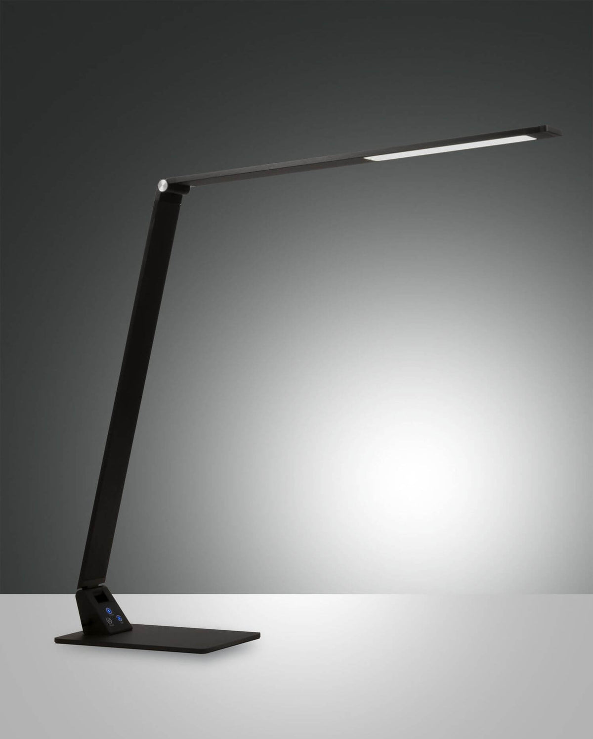 Lampe de bureau noire de profil sur fond sombre, bras articulé et faisceau lumineux