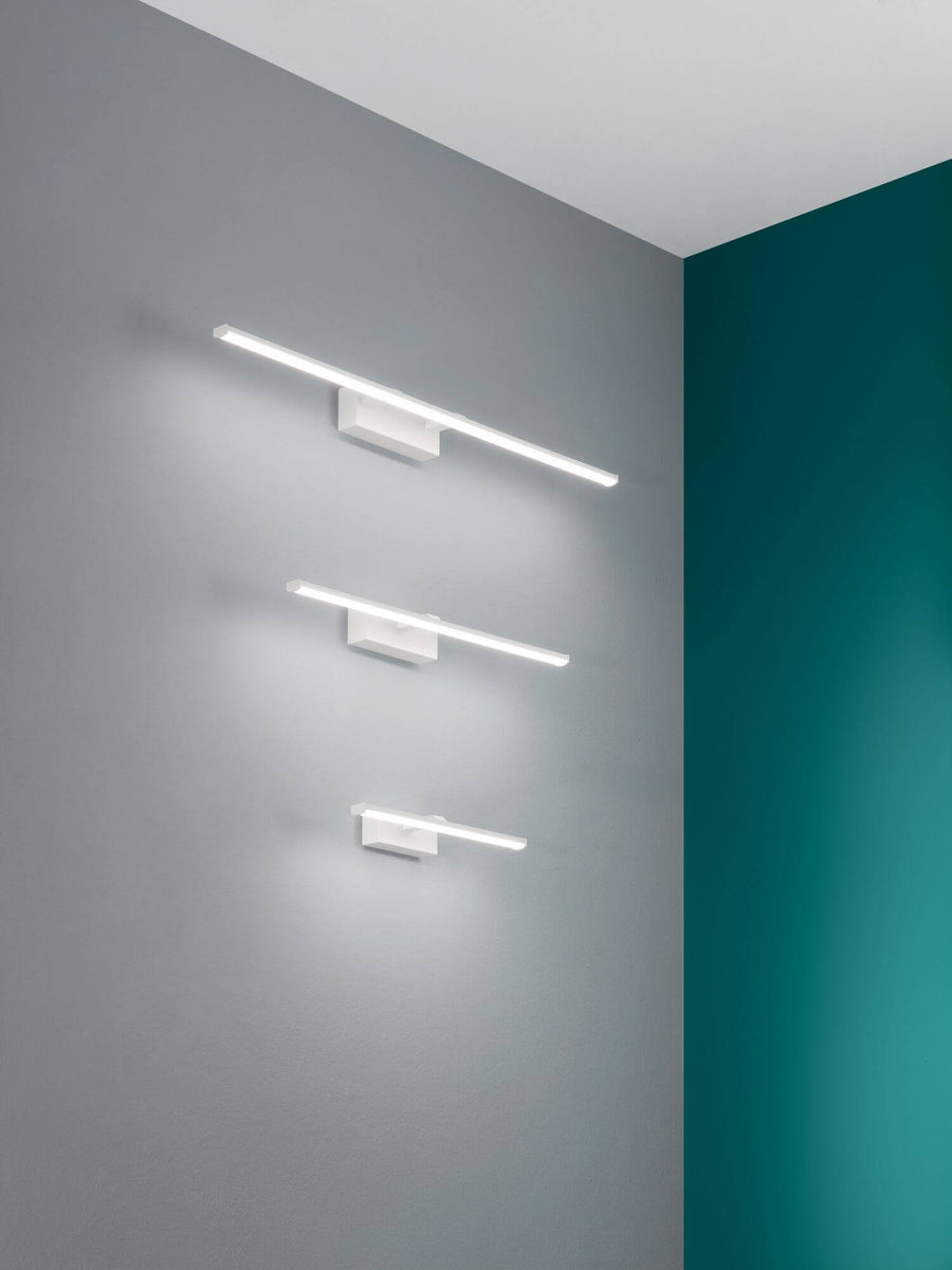Trois appliques murales blanches de tailles différentes allumées sur mur gris et bleu canard