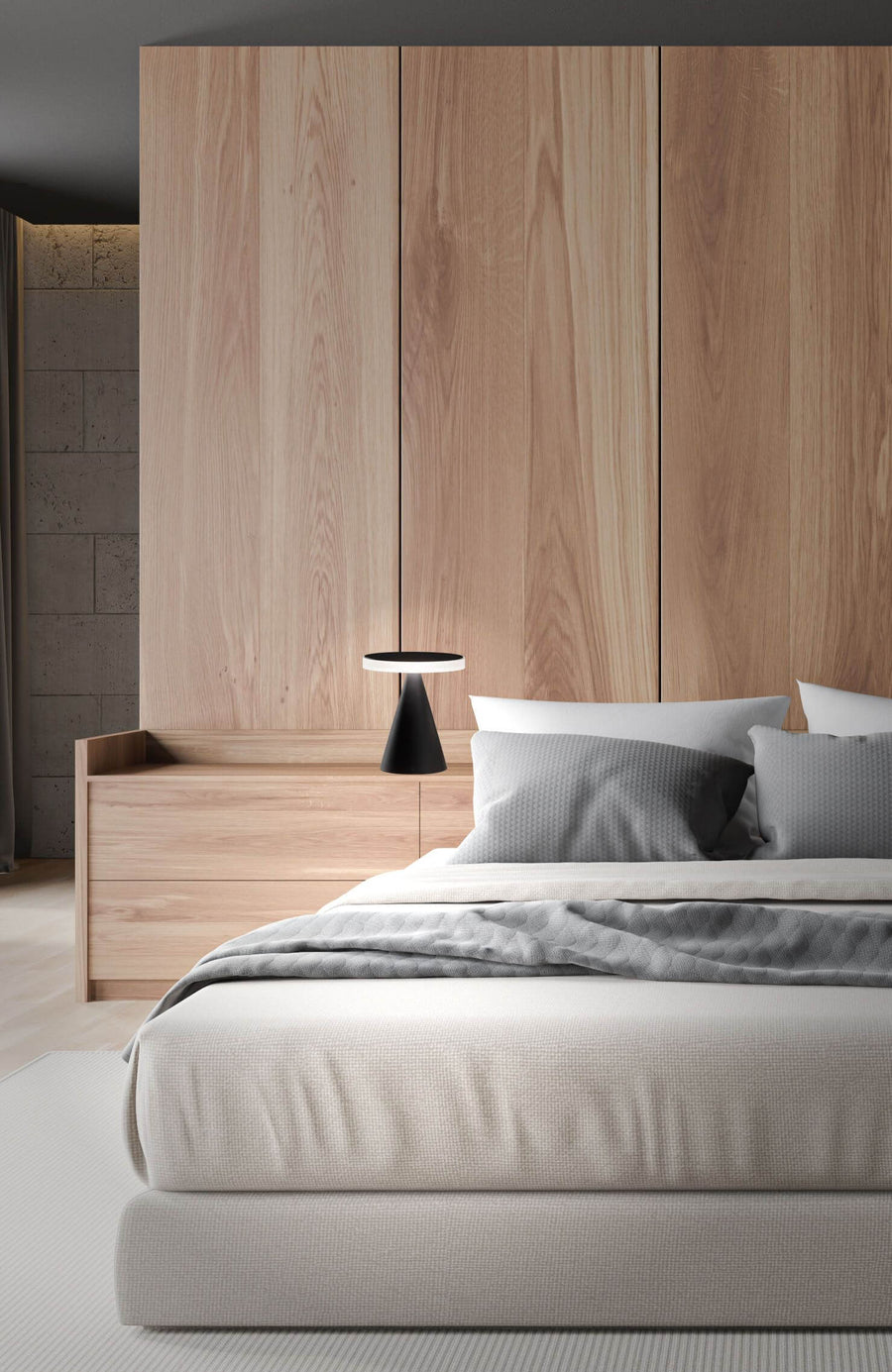 Chevet en bois avec la lampe noire allumée, chambre et lit en arrière-plan.