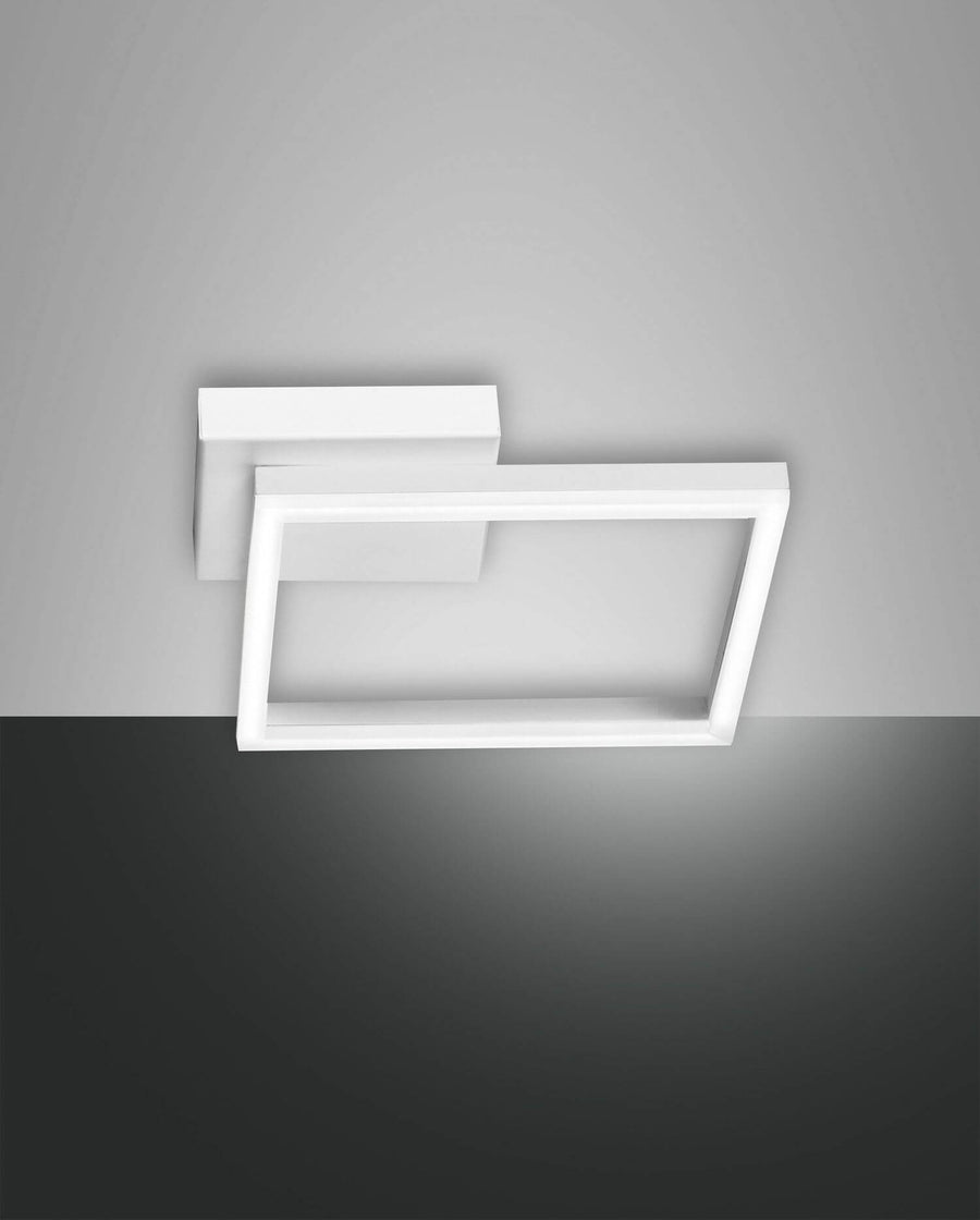 Plafonnier blanc à deux cadres rectangulaires décalés, photographié de face sur fond bicolore.