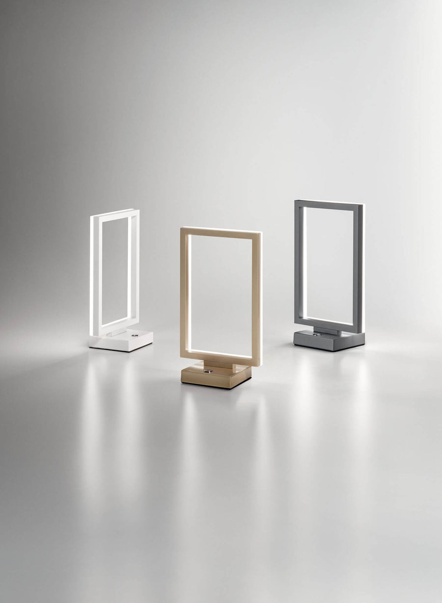 Trois lampes à poser rectangulaires : blanche, dorée et grise, alignées sur fond clair.