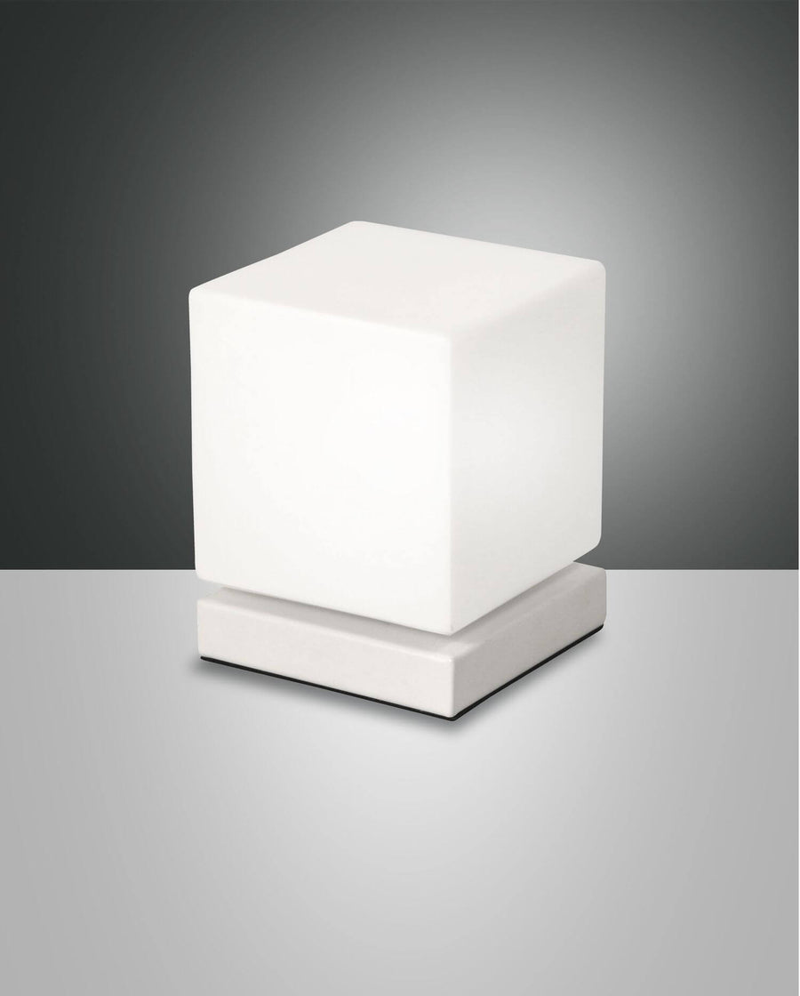 Lampe à poser cubique blanche présentée de face sur fond gris dégradé