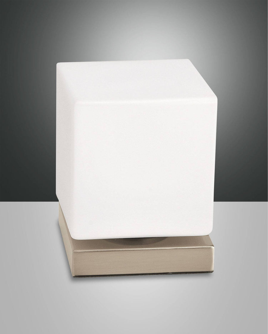 Lampe à poser de face sur fond gris, cube blanc sur socle doré