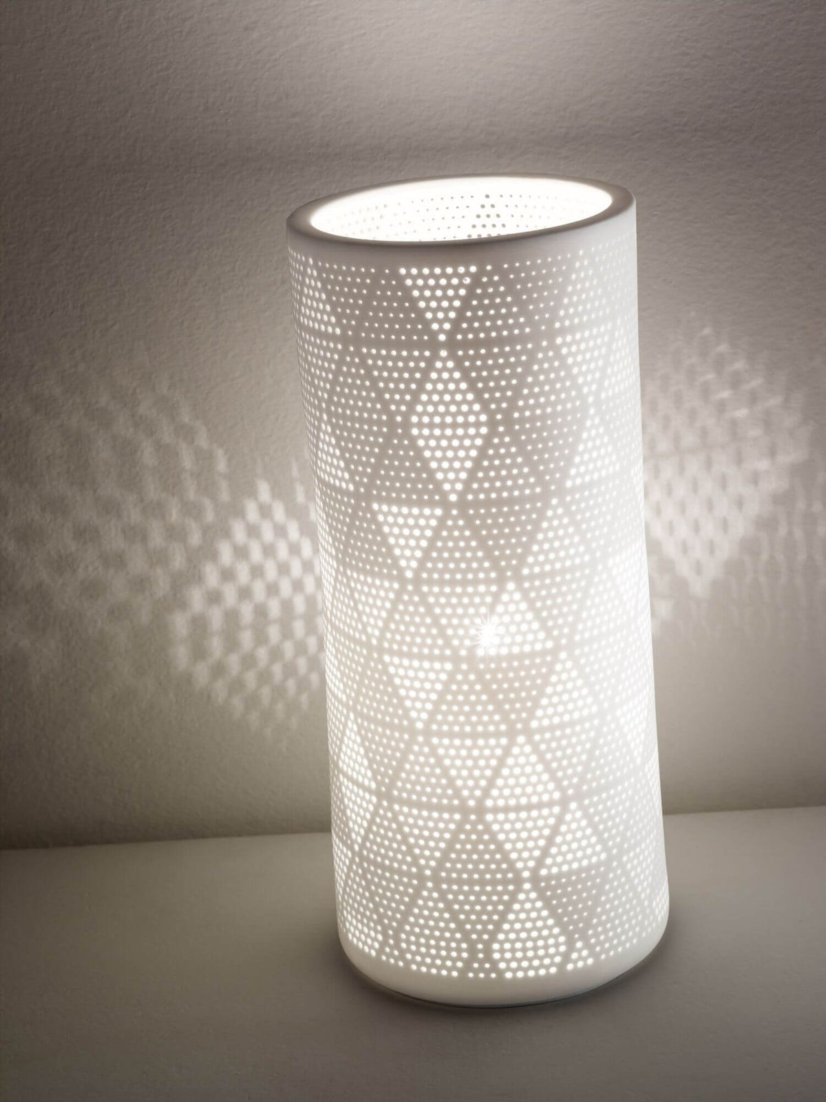 Lampe allumée contre un mur, ombres géométriques dessinées par les perforations