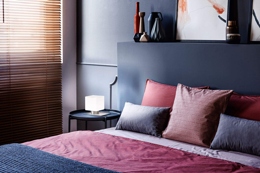 Lampe cube allumée posée sur table de nuit dans une chambre bleue et rose