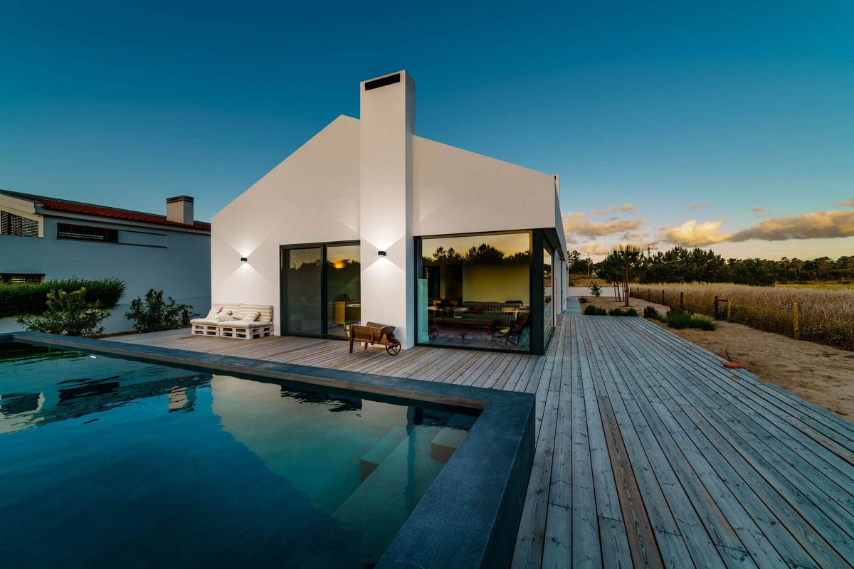 Mise en ambiance extérieure sur façade blanche avec piscine et terrasse en bois au crépuscule