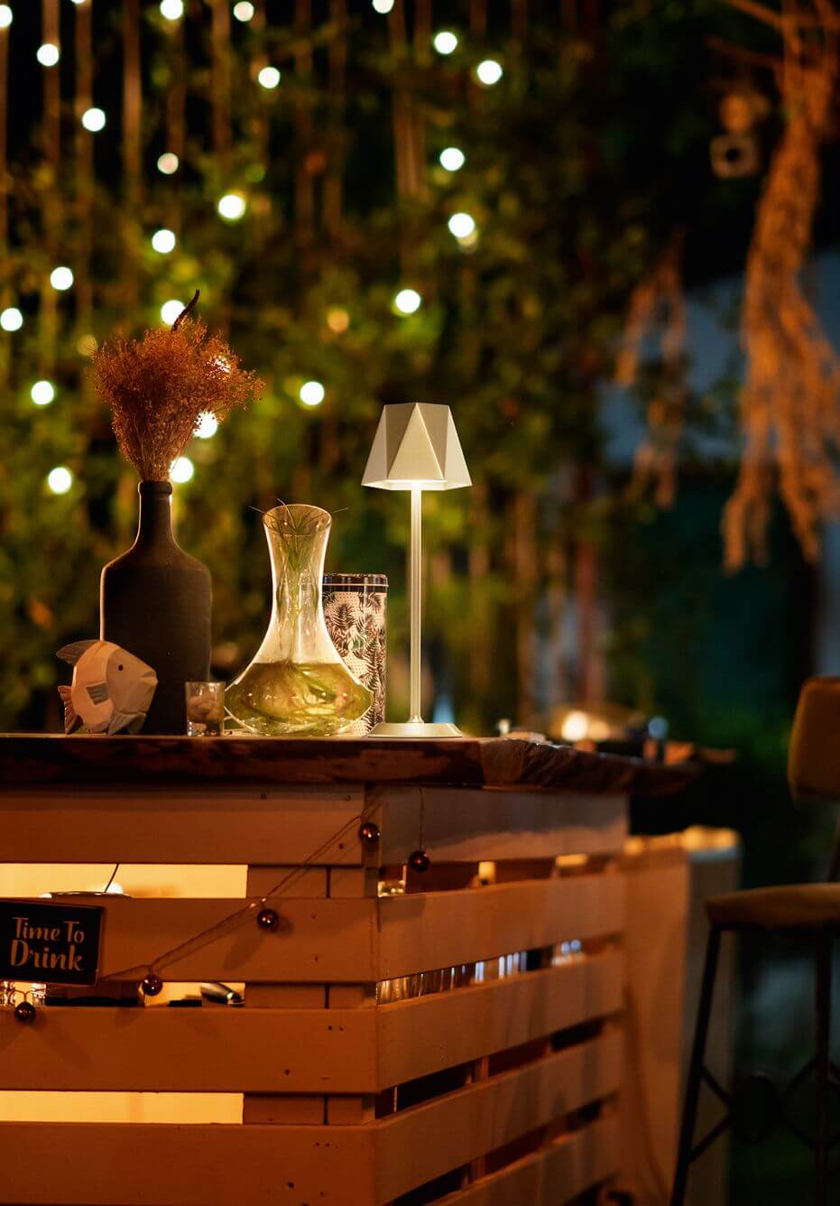 Lampe blanche allumée sur un bar en palettes, ambiance nocturne avec guirlande lumineuse