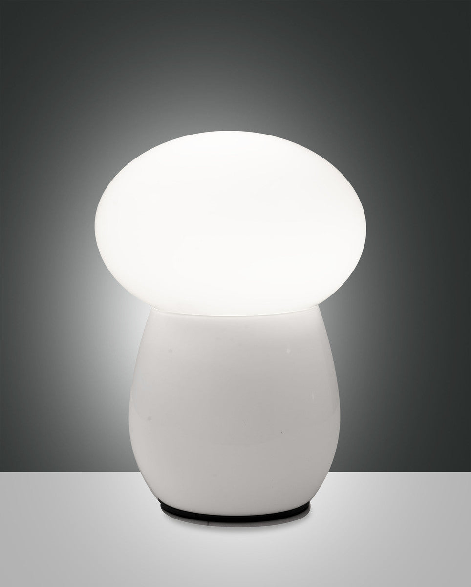 Lampe à poser blanche en verre allumée, de face sur fond gris