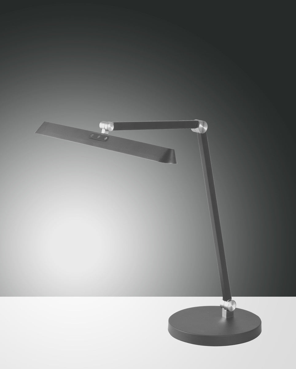 Lampe à poser anthracite inclinée, tête plate rectangulaire et base ronde.