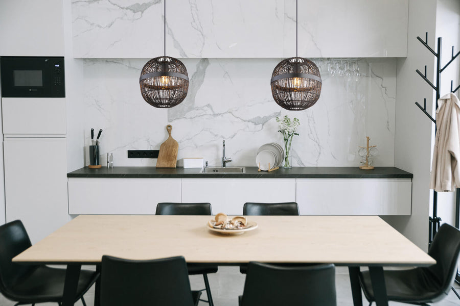 Mise en scène dans une cuisine moderne, deux suspensions noires au-dessus d'une table en bois.