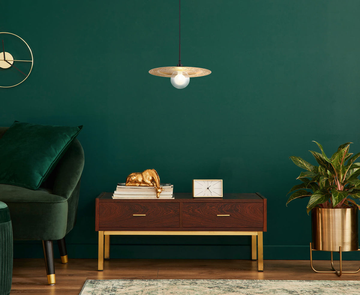 Mise en ambiance dans un intérieur vert bouteille avec suspension dorée allumée au-dessus d'un meuble