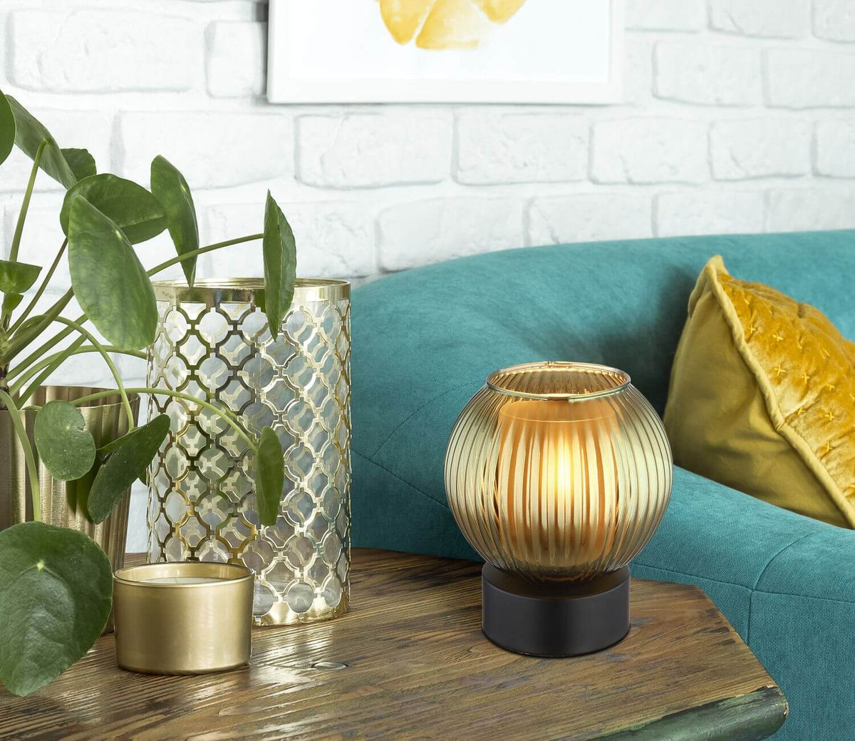 Mise en ambiance du luminaire allumé sur table en bois, canapé turquoise et coussin doré
