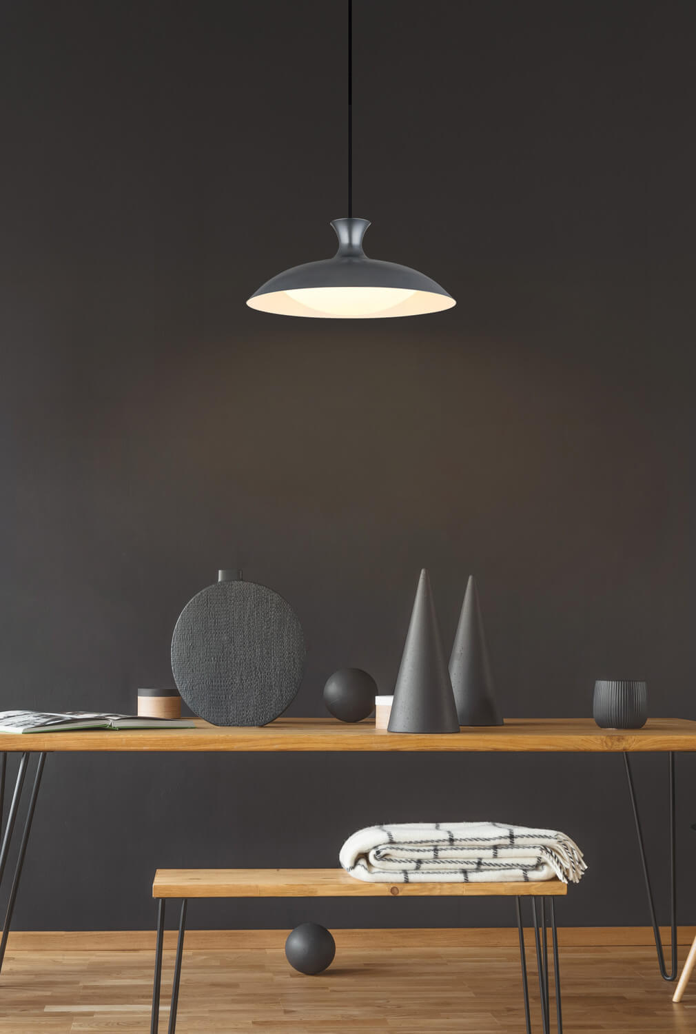 Mise en ambiance : suspension grise éclairée au-dessus d'une table en bois décorée