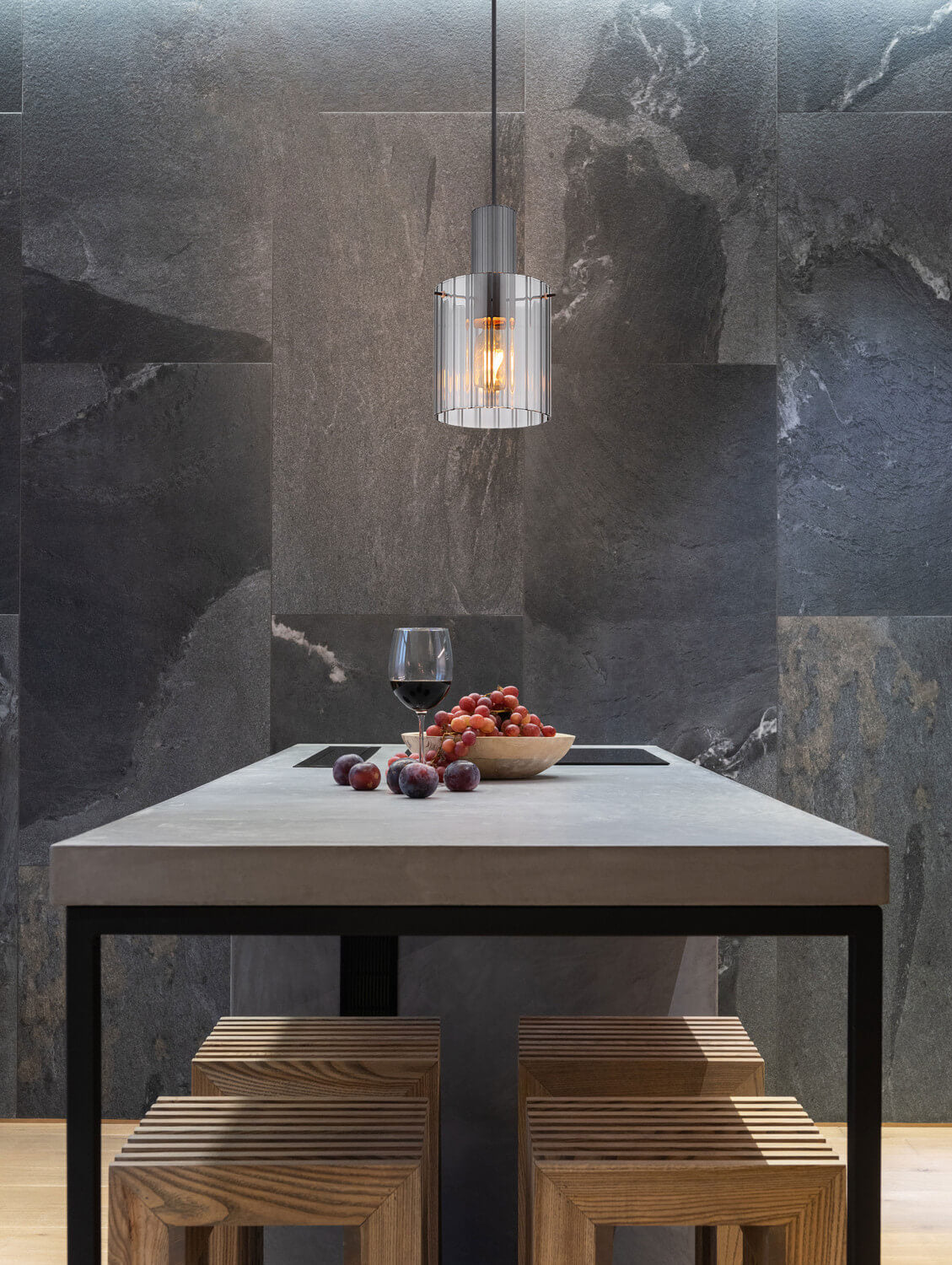 Mise en ambiance : luminaire suspendu éclairant la table en pierre et le verre de vin