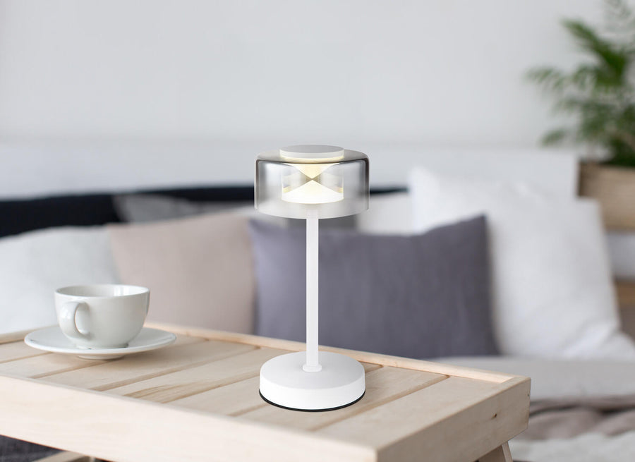 Lampe blanche posée sur une table basse en bois, près d'une tasse.