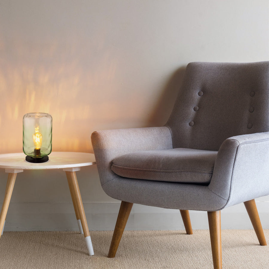 Lampe posée sur une table basse, près d’un fauteuil gris, éclairant le mur