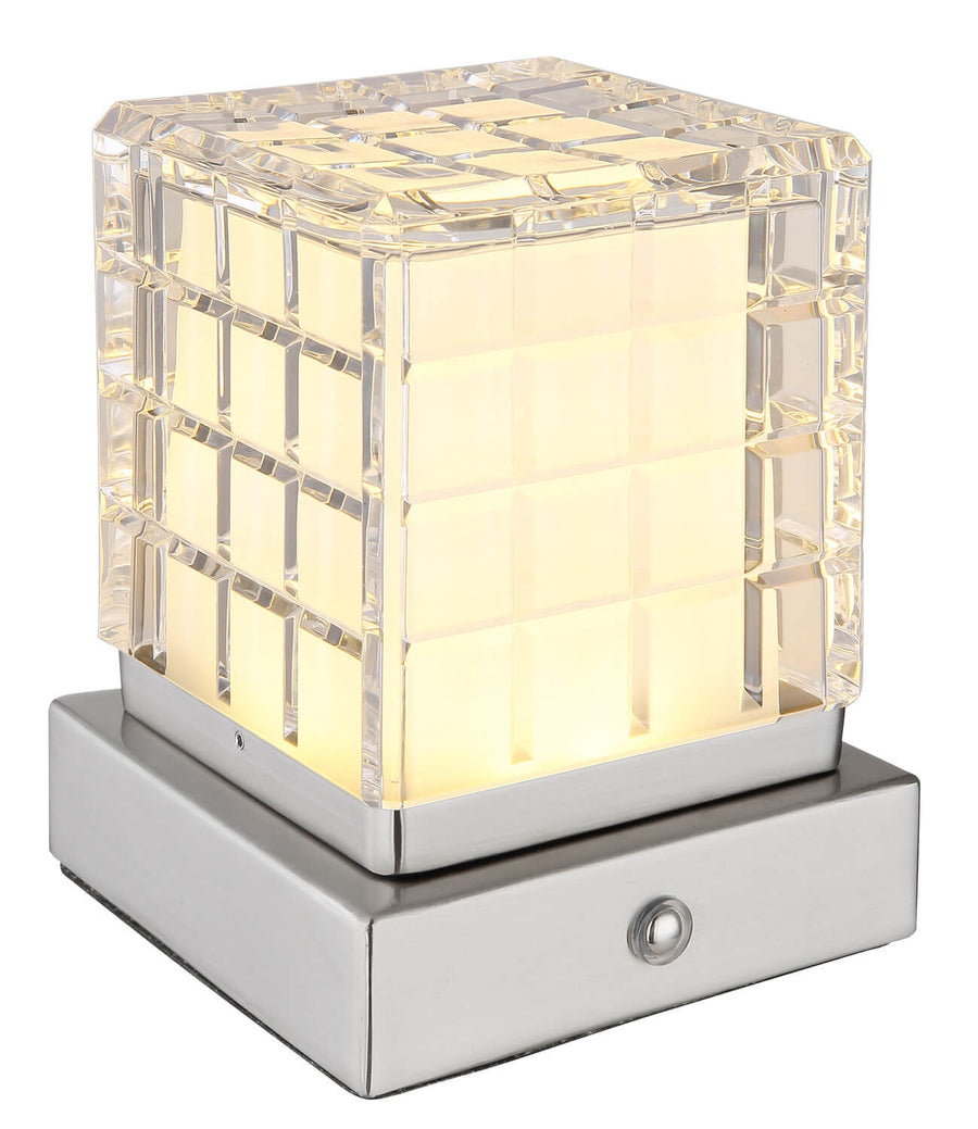 Lampe cube diffusant une lumière chaude sur sa base en nickel satiné
