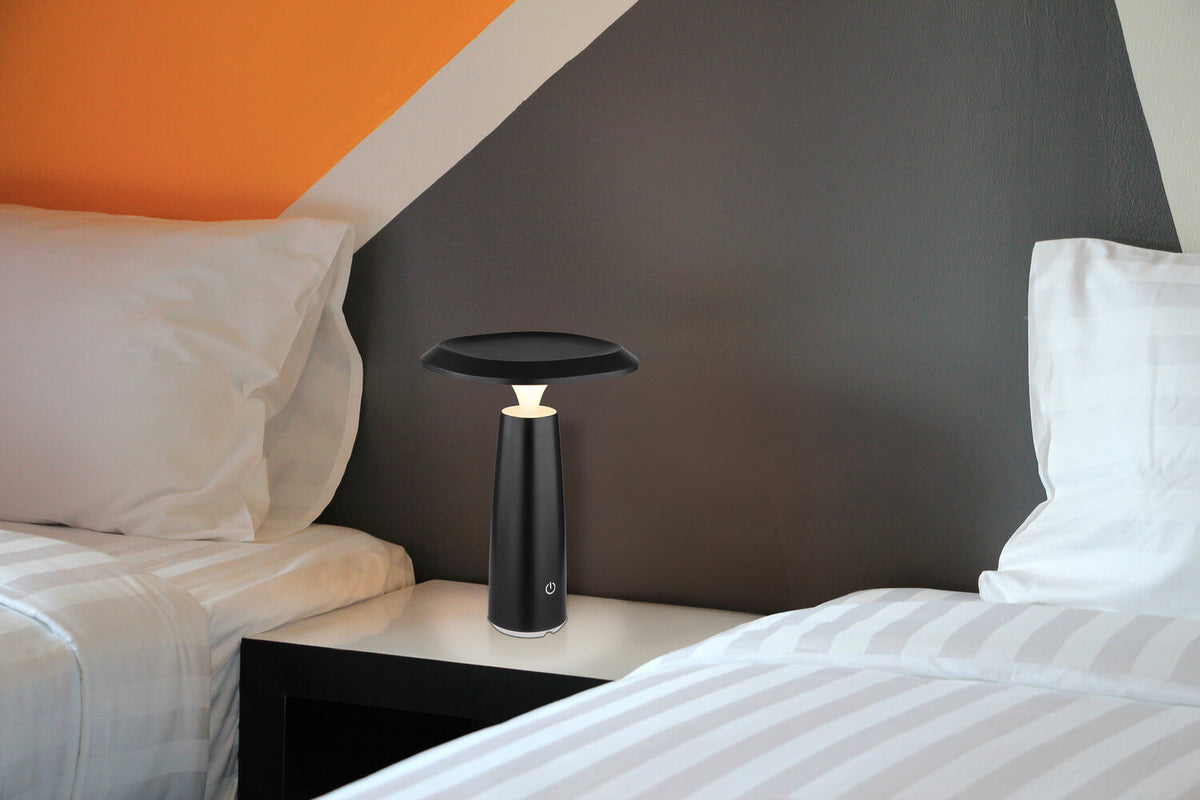 Lampe à poser allumée sur table de nuit, chambre aux murs géométriques orange et gris.