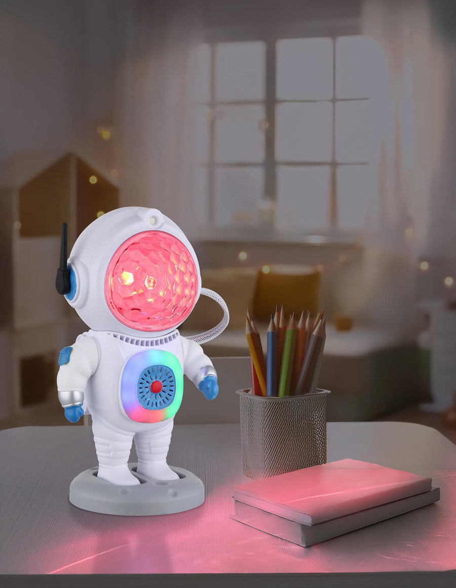 Lampe astronaute posée sur un bureau, allumée à côté de crayons et d'un livre.