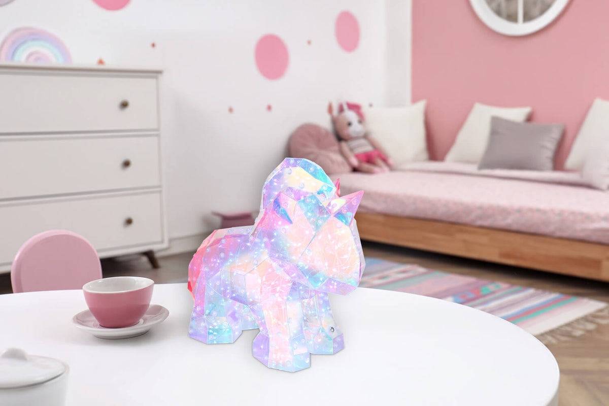 Lampe licorne posée sur table blanche dans une chambre enfantine rose.