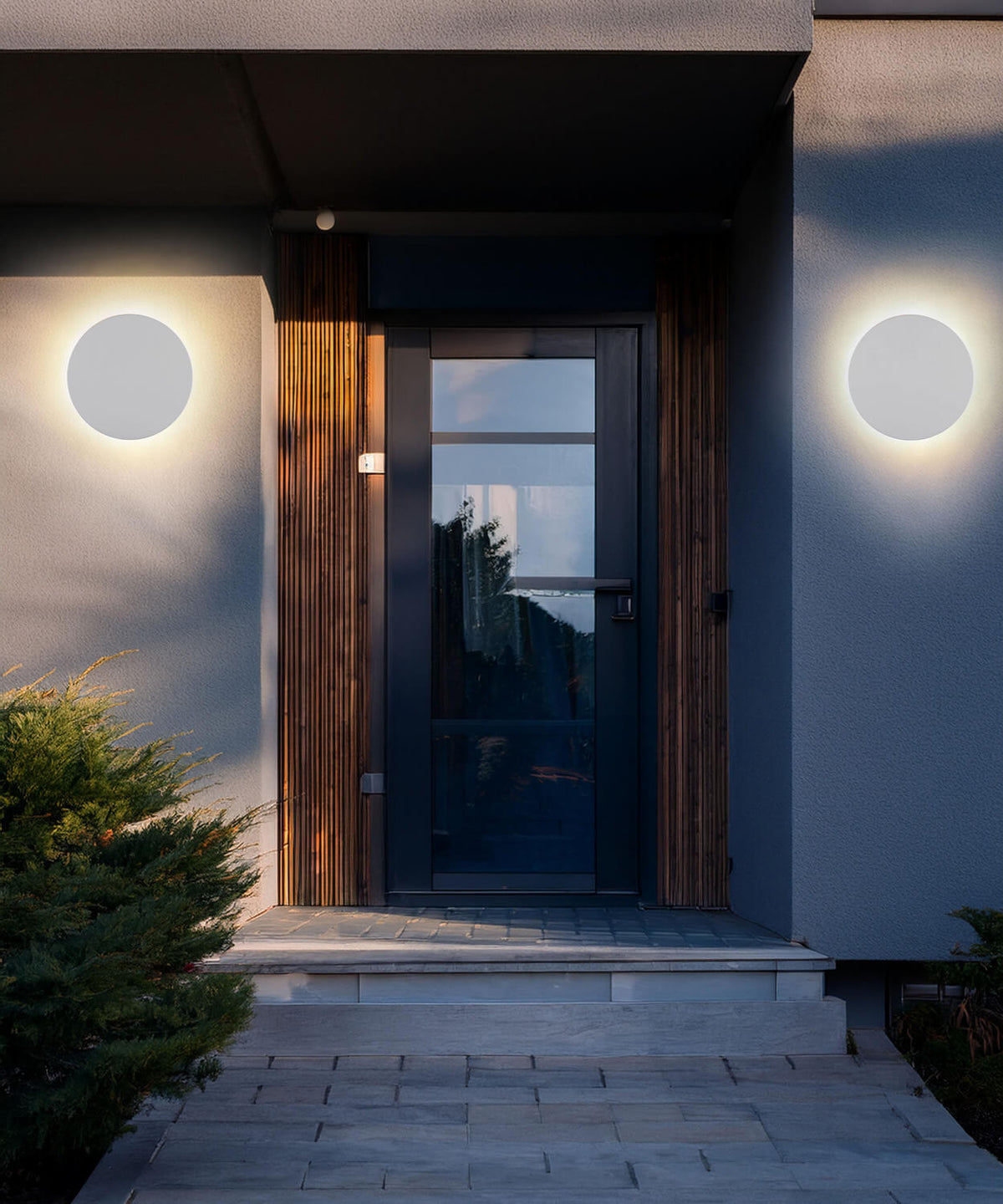 Mise en ambiance nocturne, deux appliques rondes encadrant une porte d'entrée moderne