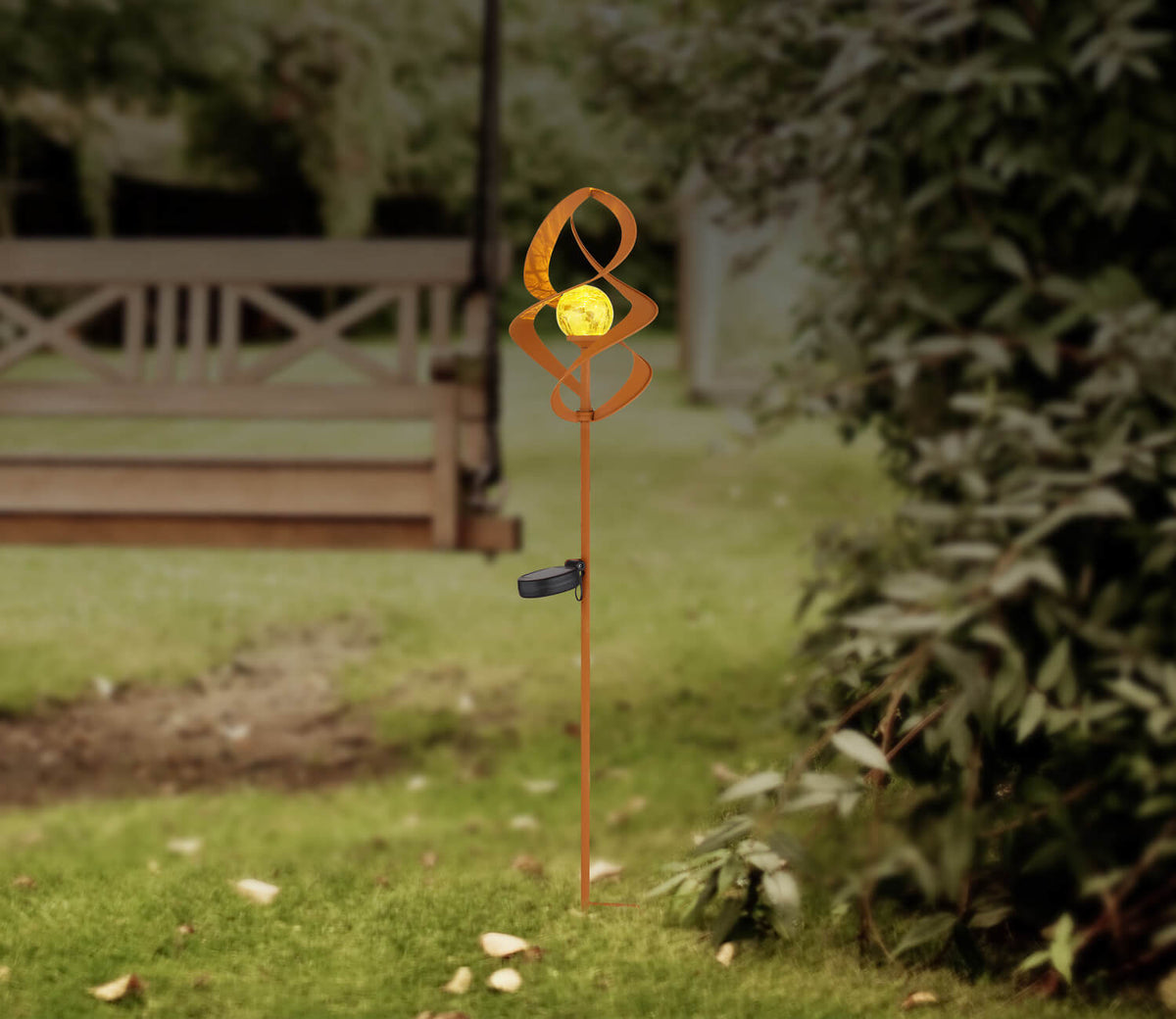 Mise en ambiance dans un jardin, luminaire planté dans la pelouse près d'un banc.