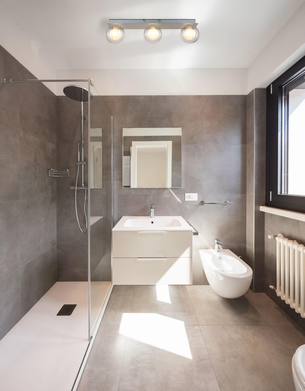 Mise en ambiance dans une salle de bain moderne avec le plafonnier allumé au-dessus du lavabo.