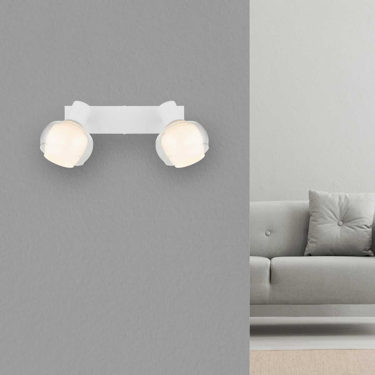 Spot double blanc mat installé au mur au-dessus d'un canapé gris, dans un salon.