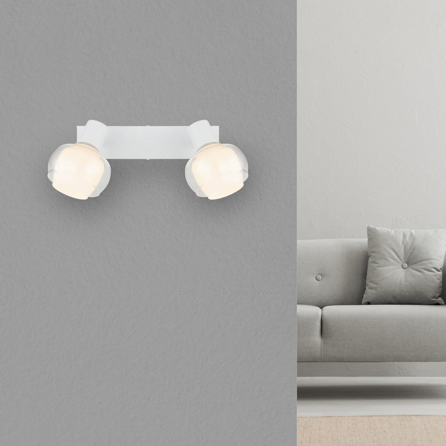 Spot double blanc mat installé au mur au-dessus d'un canapé gris, dans un salon.