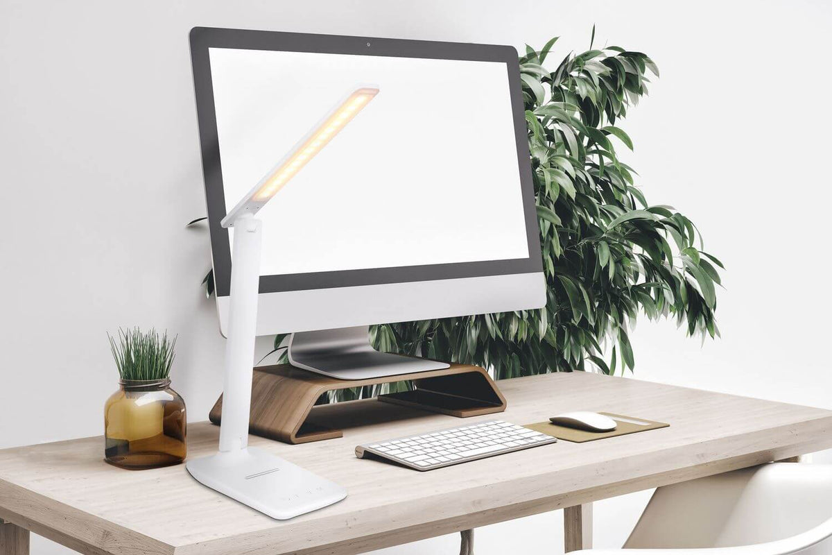 Lampe blanche allumée sur un bureau en bois près d'un ordinateur