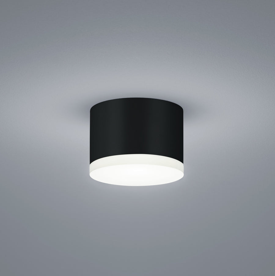 Plafonnier cylindrique noir vu de face sur fond gris clair, diffuseur blanc opalin.