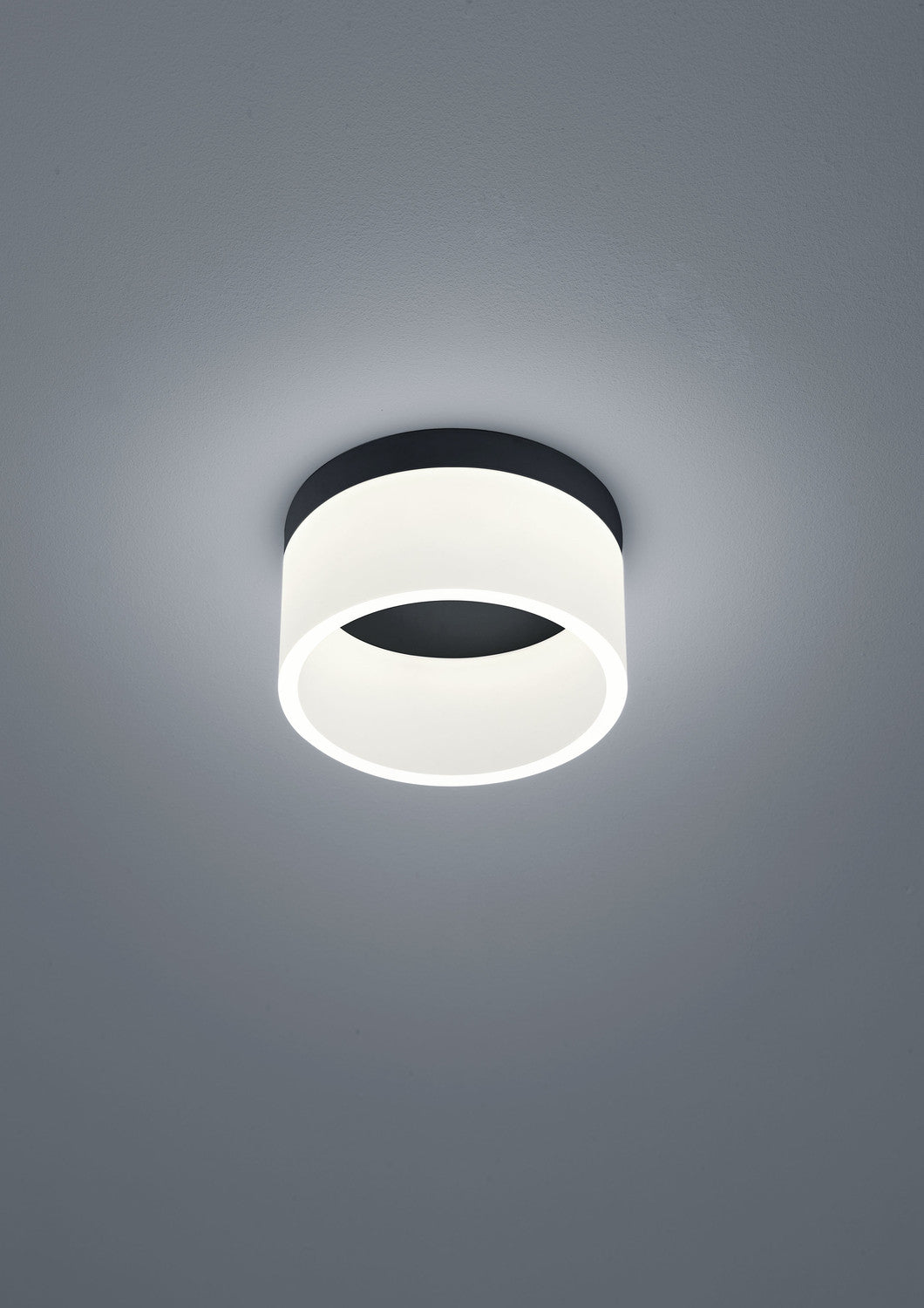 Vue rapprochée du plafonnier cylindrique noir et blanc, éclairé par en dessous.