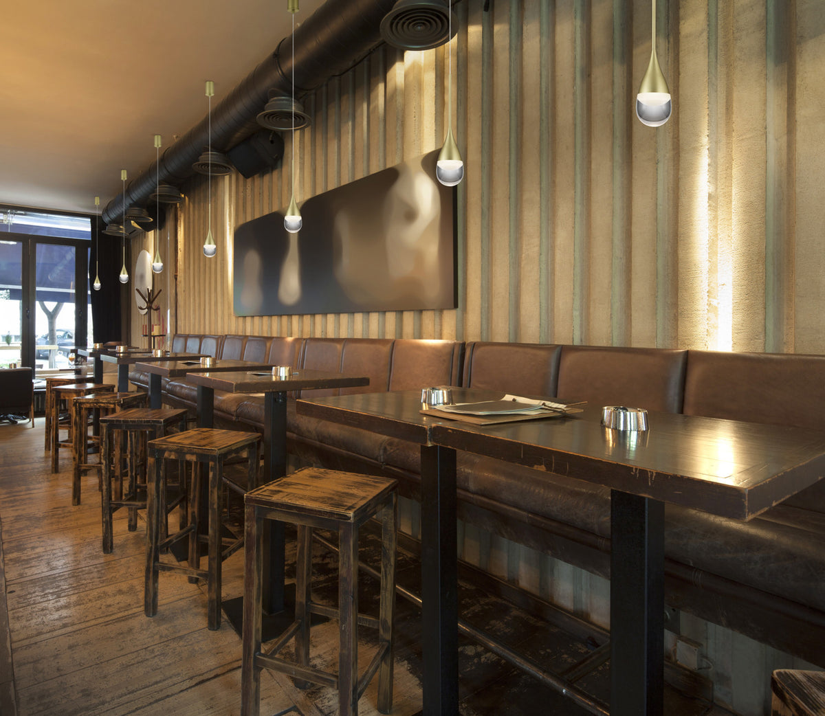 Mise en ambiance dans un bar avec plusieurs suspensions dorées au-dessus des tables