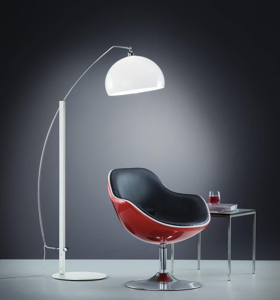 Lampadaire blanc au bras arqué éclairant un fauteuil rouge dans un décor sombre