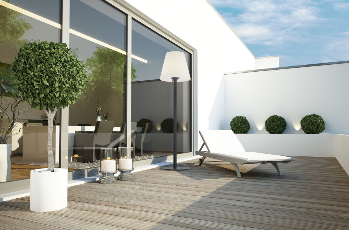 Mise en ambiance extérieure : lampadaire près d'une baie vitrée, transat et plantes.
