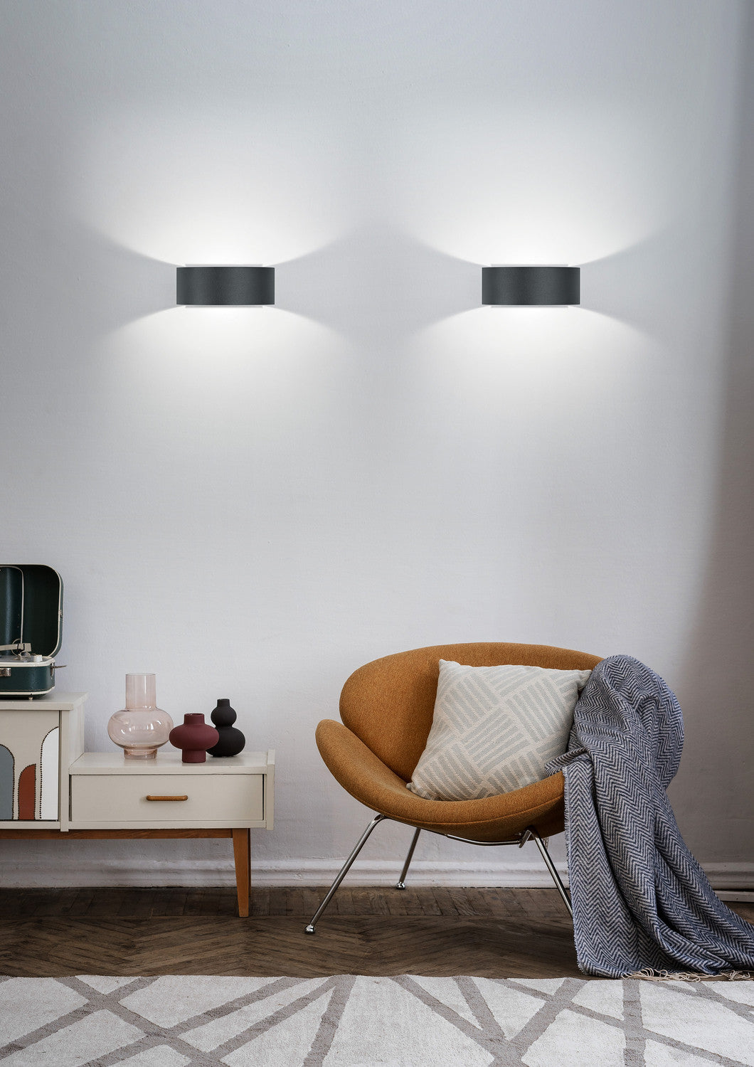 Mise en ambiance avec deux appliques noires éclairant un mur blanc au-dessus d'un fauteuil