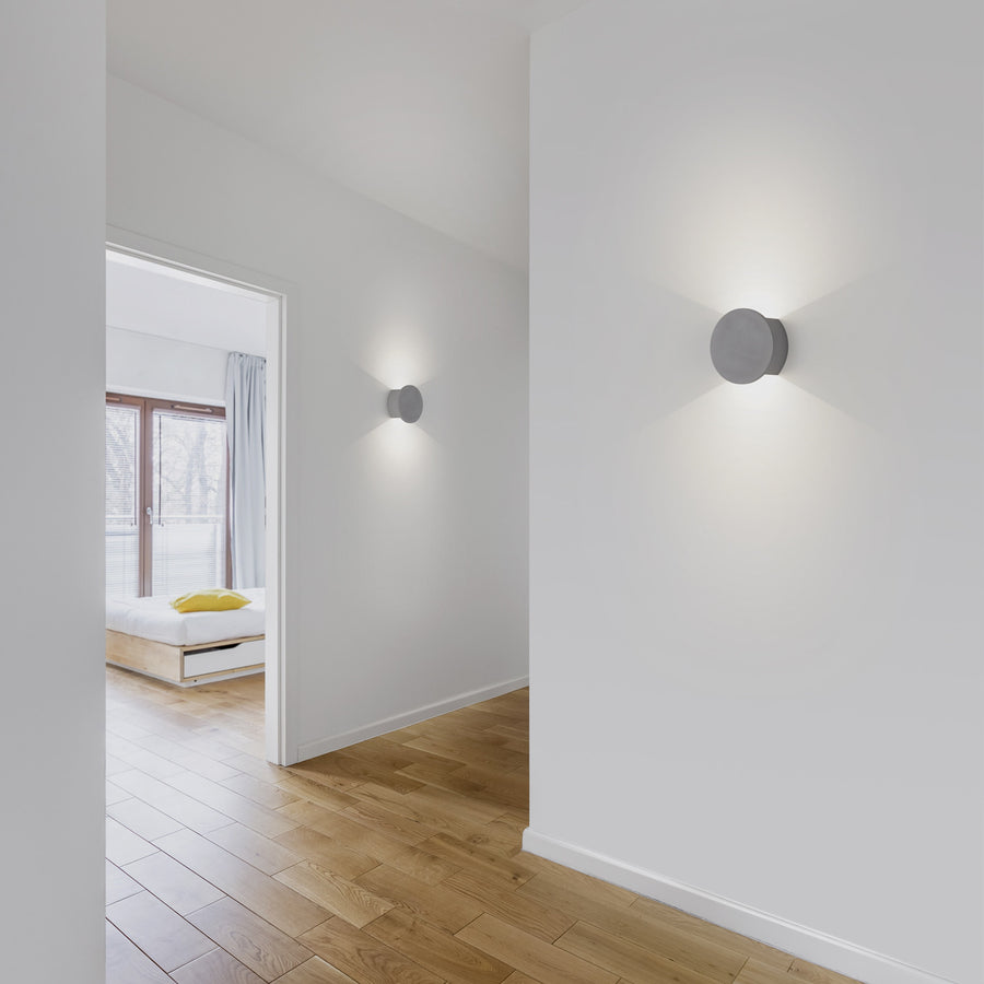 Deux appliques murales allumées éclairant un couloir blanc au parquet clair
