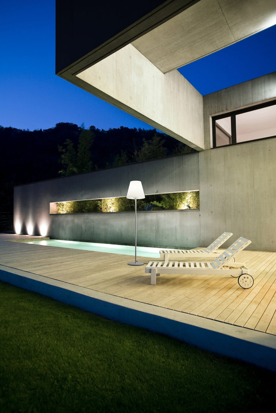 Lampadaire extérieur éclairé au bord d'une piscine en bois, crépuscule, chaises longues blanches