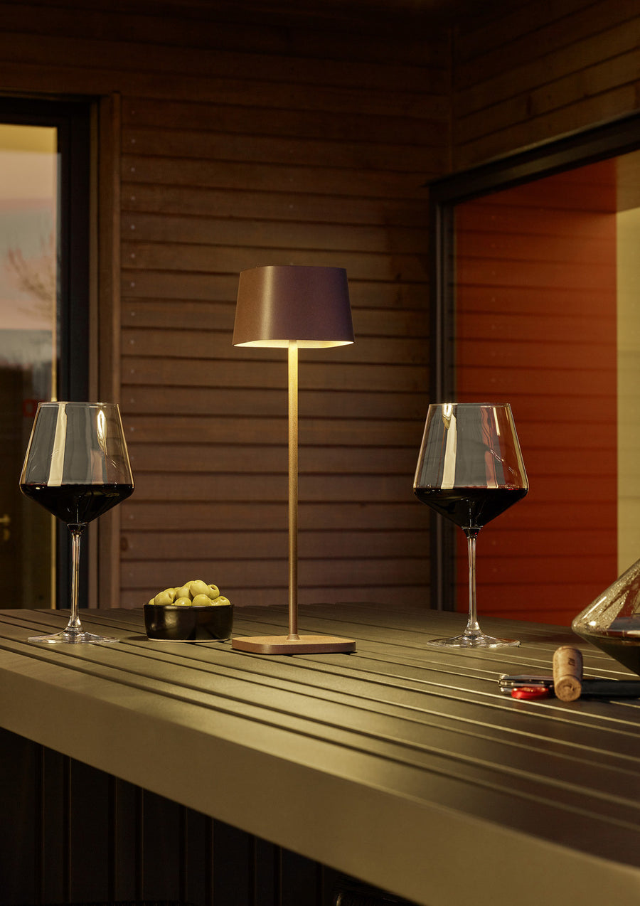 Lampe posée sur comptoir extérieur en bois, deux verres de vin rouge