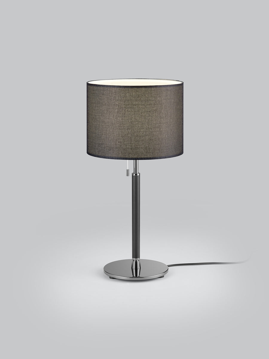 Lampe à poser noire de face sur fond gris clair, abat-jour cylindrique et socle rond.