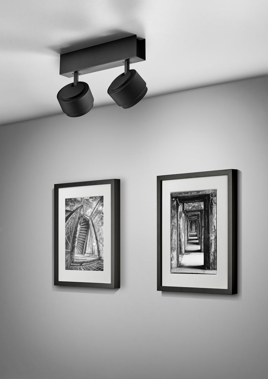 Vue en plongée du luminaire fixé au plafond face à deux tableaux encadrés.