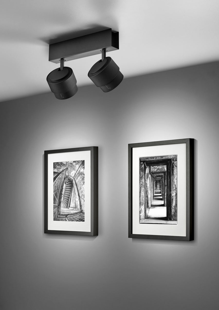 Les deux projecteurs orientables éclairent deux photographies noir et blanc dans un intérieur minimaliste.