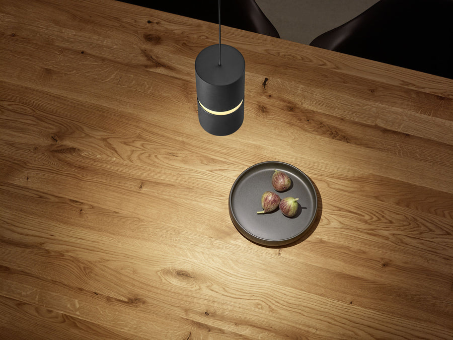 Vue plongeante d'une suspension noire éclairée au-dessus d'une table en bois avec assiette de figues.