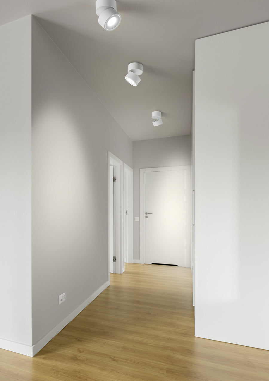 Trois plafonniers blancs orientables éclairant un couloir clair au parquet