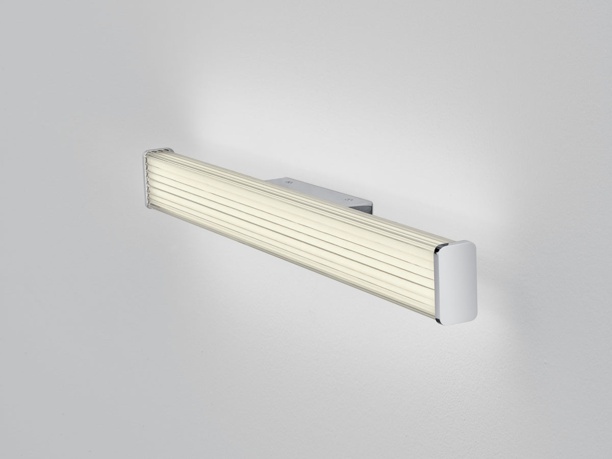 Vue de trois quarts du luminaire chromé posé sur fond gris clair, diffuseur strié crème.
