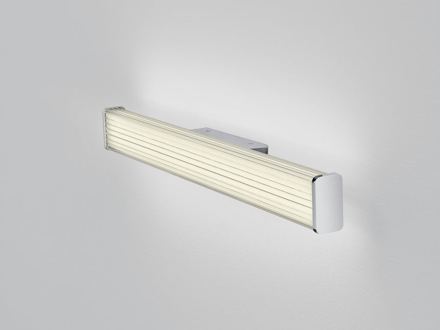 Vue de trois quarts du luminaire chromé posé sur fond gris clair, diffuseur strié crème.