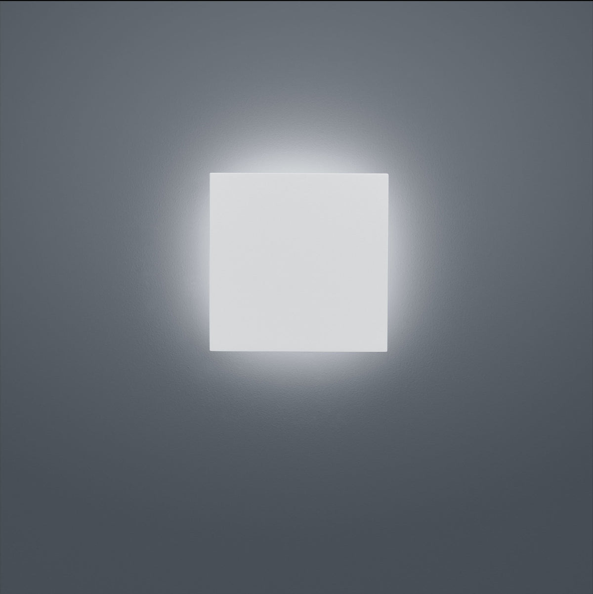 Face avant du luminaire carré blanc allumé, halo lumineux diffus sur mur gris