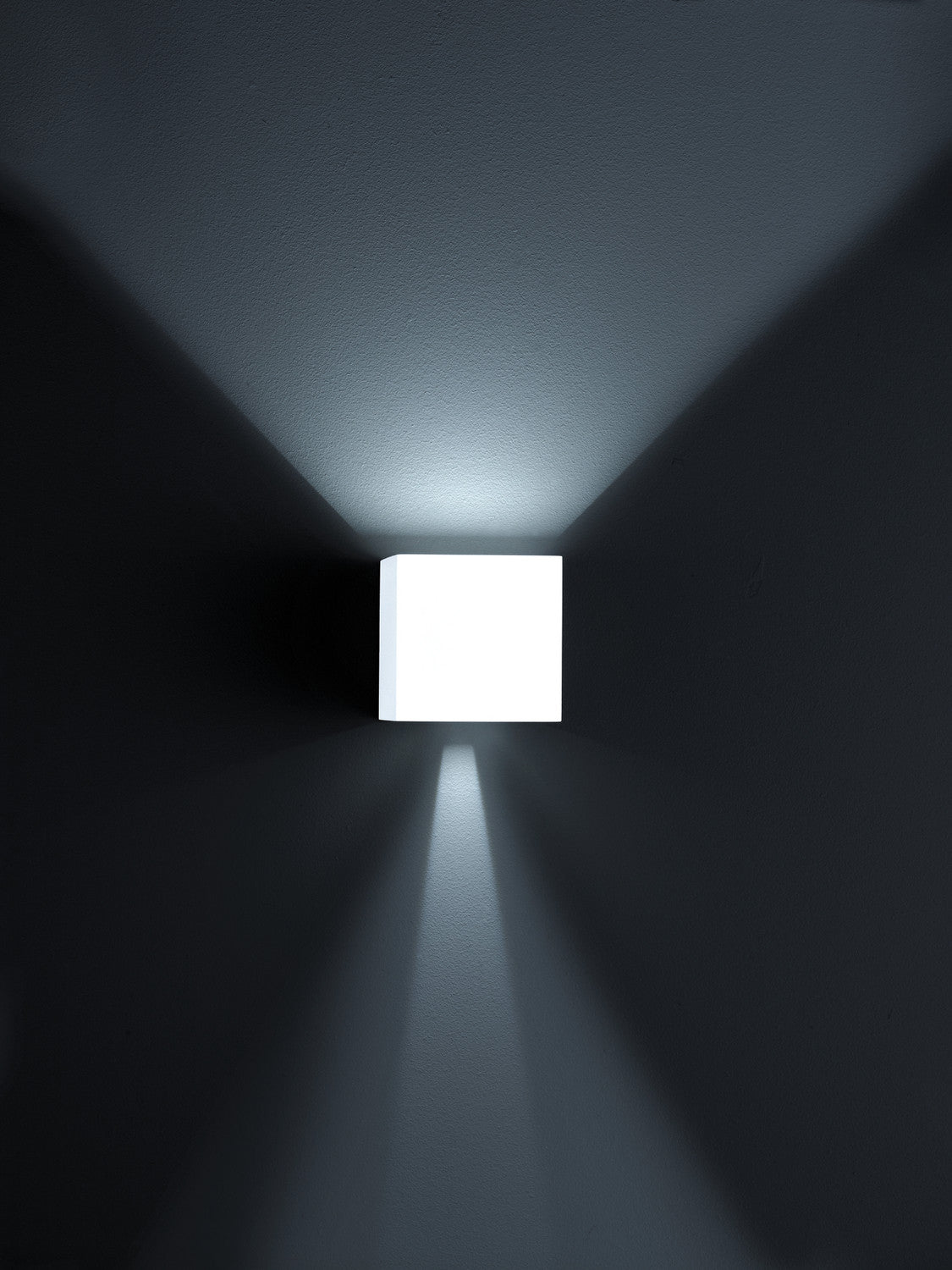 Applique murale cube blanche allumée seule dans la pénombre, éclairant vers le haut et le bas